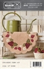 This picture shows a strawberry penny mat with fresh berries and blossoms set in a charming kitchen, with a watering can to remind us how fresh the wool mat feels.